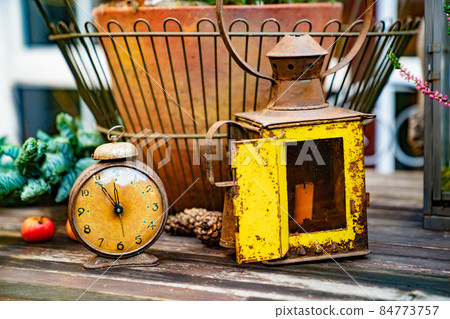 an antique clock and a lantern on the background of a flower pot. an antique clock and a lantern on the background of a flower pot. 84773757
