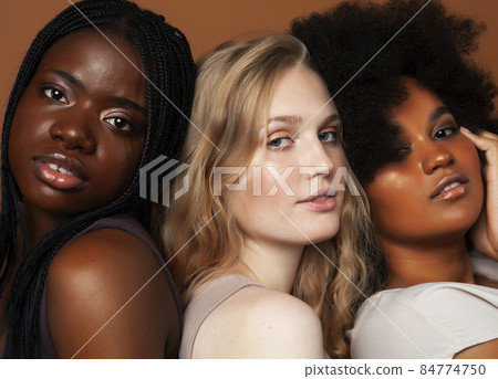 young pretty african and caucasian women posing cheerful together on brown background, lifestyle diverse nationality people concept 84774750