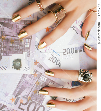 hands of rich woman with golden manicure and many jewelry rings on cash euros hands of rich woman with golden manicure and many jewelry rings on cash euros 84774764
