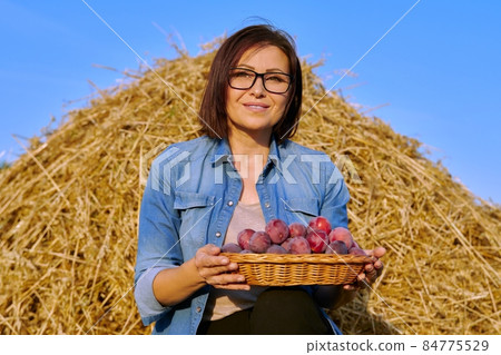 Summer rural woman portrait with basket of plums, dry hay sky background 84775529