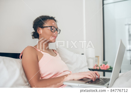 A dark-skinned womant typing on laptop while staying in bed 84776712