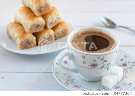 A cup of frothy coffee and a plate of baklava for breakfast. A cup of frothy coffee and a plate of baklava for breakfast. 84777304
