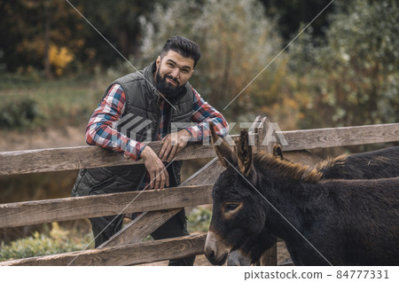 Dark-haired young farmer standing near the cattle-pen 84777331