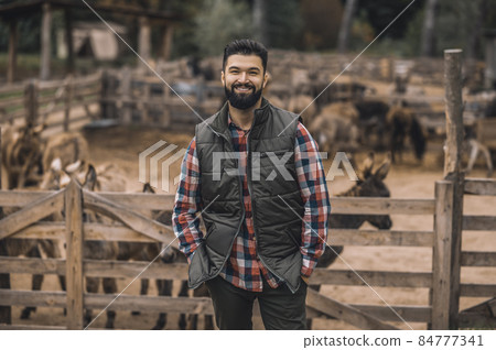 A farmer in the black vest and a plaid shirt standing near the cattle-pen A farmer in the black vest and a plaid shirt standing near the cattle-pen 84777341