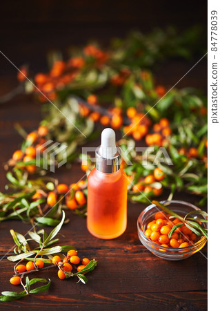Glass bottle with sea buckthorn oil berries and sea buckthorn branches on wooden background 84778039