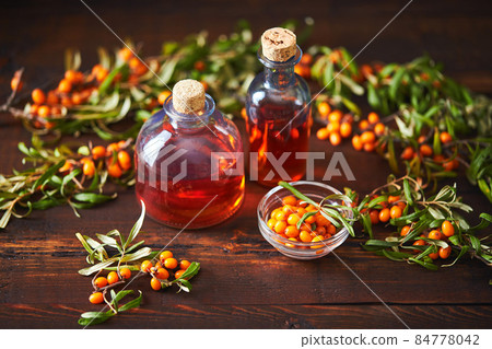 Glass bottle with sea buckthorn oil berries and sea buckthorn branches on wooden background Glass bottle with sea buckthorn oil berries and sea buckthorn branches on wooden background 84778042