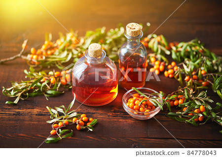 Glass bottle with sea buckthorn oil berries and sea buckthorn branches on wooden background Glass bottle with sea buckthorn oil berries and sea buckthorn branches on wooden background 84778043