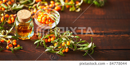 Glass bottle with sea buckthorn oil berries and sea buckthorn branches on wooden background Glass bottle with sea buckthorn oil berries and sea buckthorn branches on wooden background 84778044