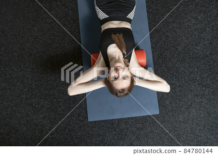 Young sports girl lies on MFR rollers. Woman does back massage with myofascial roll. Myofascial release. Top view Young sports girl lies on MFR rollers. Woman does back massage with myofascial roll. Myofascial release. Top view 84780144
