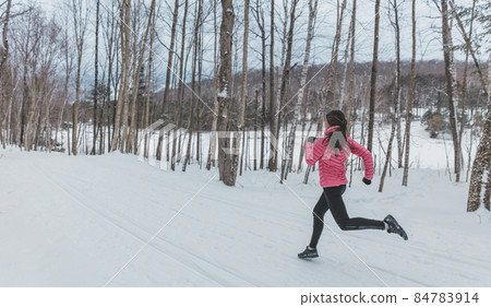 Woman Running in Winter Snow. Runner jogging outside on cold winter day in forest. Fit healthy lifestyle photo with beautiful young fitness model. Girl running in full length in winter running shoes 84783914