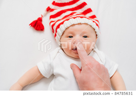 hand touches face of cute little kid in cap of Christmas elf or gnome.baby santa hand touches face of cute little kid in cap of Christmas elf or gnome.baby santa 84785631