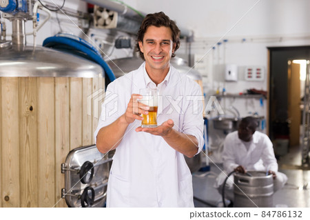 Man brewer in uniform is standing with glass of two type of beer Man brewer in uniform is standing with glass of two type of beer 84786132