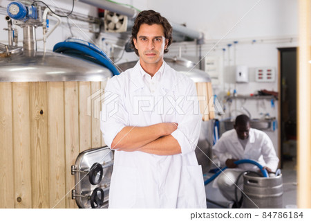 Young man brewer in uniform is standing with glass of beer 84786184