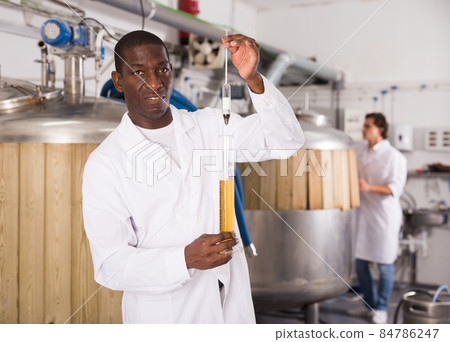 Young man brewer checking quality of beer in flask in brew-house 84786247