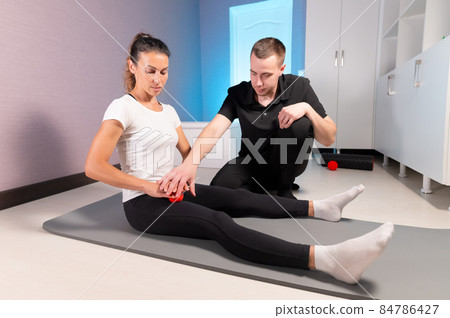 Myofascial release. A male physiotherapist places a ball for the rehabilitation of the client's leg muscles while sitting technique using a red ball. Self-massage concept. Practical use. 84786427