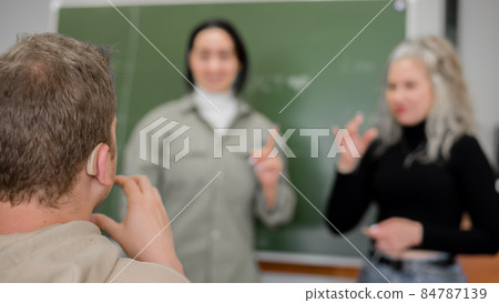Two girls and a guy are talking in sign language. Three deaf students chatting in a university classroom. Two girls and a guy are talking in sign language. Three deaf students chatting in a university classroom. 84787139