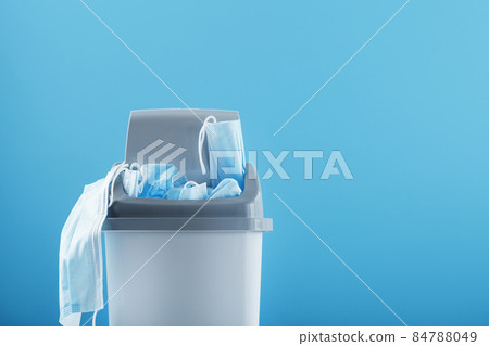Waste bin full of used protective masks on a light blue background with free space. Waste bin full of used protective masks on a light blue background with free space. 84788049