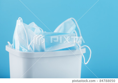 A white trash can full of virus protection masks on a blue background. A white trash can full of virus protection masks on a blue background. 84788050