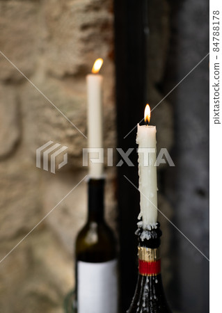 Candles burn in wine and champagne bottles on the windowsill. Front view. 84788178