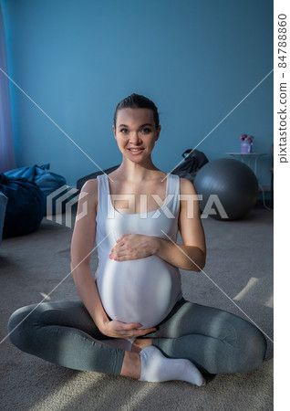 A pregnant girl sits in a lotus position and holds on to her stomach. A woman is doing yoga in the 3rd trimester. A bubbling mom is waiting. A pregnant girl sits in a lotus position and holds on to her stomach. A woman is doing yoga in the 3rd trimester. A bubbling mom is waiting. 84788860