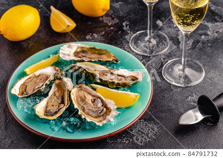 Opened fresh oysters on a blue plate, served with lemon and ice. Opened fresh oysters on a blue plate, served with lemon and ice. 84791732