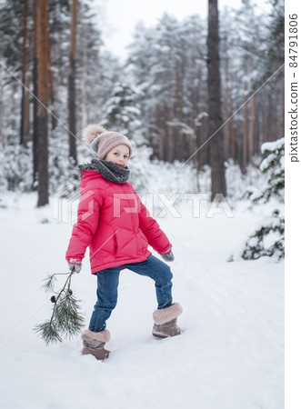 Little girl in a bright jacket plays in the winter forest 84791806