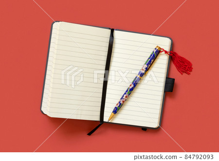 Opened ruled notebook with a ethnic pen on red table top view. Textbook mockup 84792093