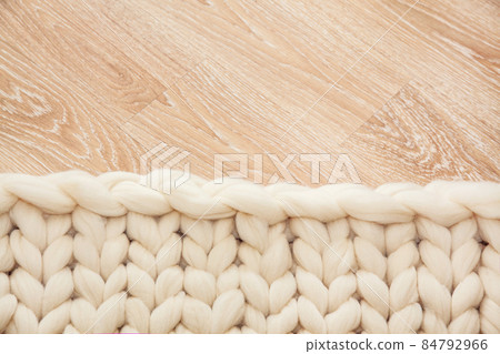 Knitted plaid of large knitting made of merino wool on wooden floor. Knitted plaid of large knitting made of merino wool on wooden floor. 84792966