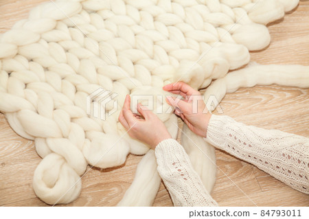 Women's hands knit a plaid of merino wool of large knitting on a wooden floor, top view flat lay. Master class step by step, training Women's hands knit a plaid of merino wool of large knitting on a wooden floor, top view flat lay. Master class step by step, training 84793011