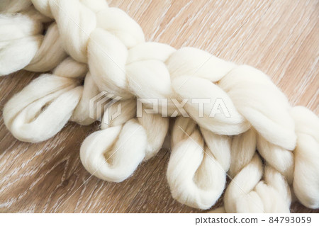 The process of knitting a plaid of large knitting from merino wool. Unfinished work with open loops on wooden floor The process of knitting a plaid of large knitting from merino wool. Unfinished work with open loops on wooden floor 84793059