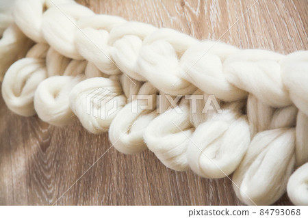 The process of knitting a plaid of large knitting from merino wool. Unfinished work with open loops on wooden floor The process of knitting a plaid of large knitting from merino wool. Unfinished work with open loops on wooden floor 84793068
