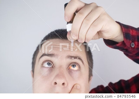 Close-up of eye drops. Artificial tear. Pain in the eyes. Sensation of grit in the eyes. A man looks out from behind a computer monitor or laptop. Drip my own eye medicine Close-up of eye drops. Artificial tear. Pain in the eyes. Sensation of grit in the eyes. A man looks out from behind a computer monitor or laptop. Drip my own eye medicine 84793546