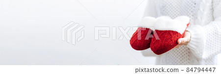 Woman in white sweater holds warm knitted red slippers. Concept of home family cozy holiday Christmas New Year. 84794447
