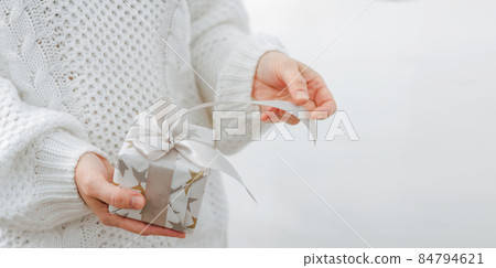 Female hands are holding small gift box. Winter holidays concept New Year Christmas. Selective focus, light background Female hands are holding small gift box. Winter holidays concept New Year Christmas. Selective focus, light background 84794621