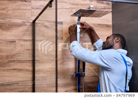 African Professional handyman working in shower bath indoors, side view portrait African Professional handyman working in shower bath indoors, side view portrait 84797969