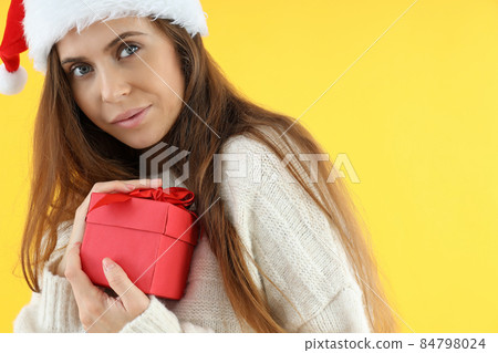 Attractive woman in Santa hat holds gift box on yellow background Attractive woman in Santa hat holds gift box on yellow background 84798024