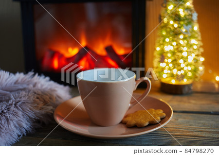 Cup with blanket over fireplace on wooden table. Winter and Christmas holiday concept Cup with blanket over fireplace on wooden table. Winter and Christmas holiday concept 84798270