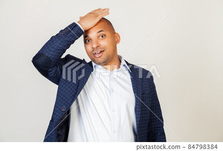 Young African American man smiling positively, resting his hand on his head for a mistake, remember Young African American man smiling positively, resting his hand on his head for a mistake, remember 84798384