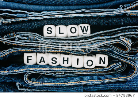 Slow fashion, second hand, Vintage Shopping, slow fashion, Sustainable fashion concept. Stack of blue old denim jeans with the words slow fashion Slow fashion, second hand, Vintage Shopping, slow fashion, Sustainable fashion concept. Stack of blue old denim jeans with the words slow fashion 84798967