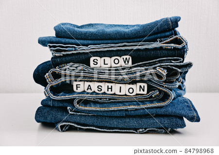 Slow fashion, second hand, Vintage Shopping, slow fashion, Sustainable fashion concept. Stack of blue old denim jeans with the words slow fashion Slow fashion, second hand, Vintage Shopping, slow fashion, Sustainable fashion concept. Stack of blue old denim jeans with the words slow fashion 84798968