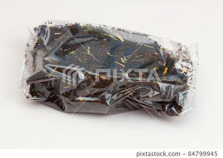 Black tea packaging on a white background. Long leaf tea with rose hips, apples and flower petals, packed in a transparent package. Tea with a fruity aroma. Isolated. Tea Packaging Concept. Close-up Black tea packaging on a white background. Long leaf tea with rose hips, apples and flower petals, packed in a transparent package. Tea with a fruity aroma. Isolated. Tea Packaging Concept. Close-up 84799945