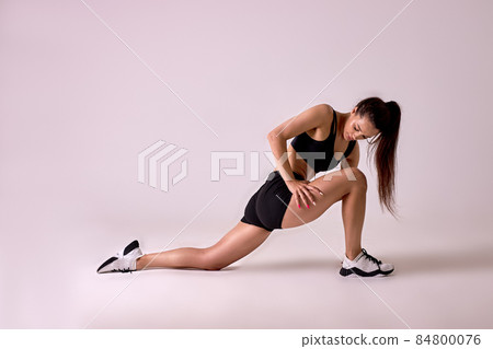 Side view of young brunette lady stretching legs before workout, isolated in studio Side view of young brunette lady stretching legs before workout, isolated in studio 84800076