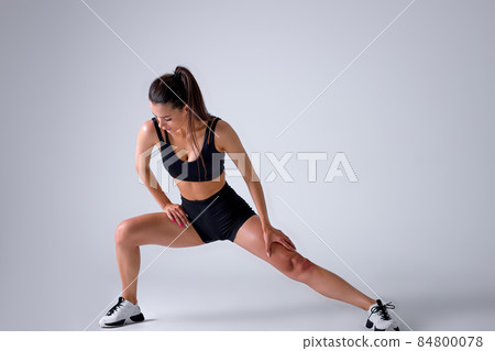 young caucasian woman coach in sporty black short top and gym shorts makes lunges young caucasian woman coach in sporty black short top and gym shorts makes lunges 84800078
