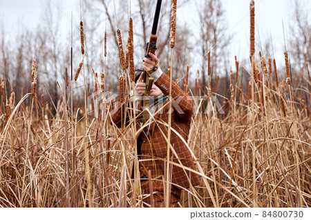 Hunter man. Shooter sighting in bird at sky. Hunting period. Male with gun in field. 84800730