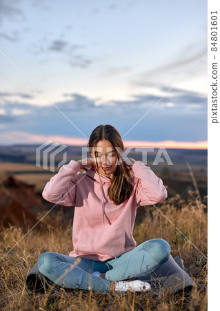 young woman is engaged in yoga, sitting on fitness mat outdoors. wellbeing concept young woman is engaged in yoga, sitting on fitness mat outdoors. wellbeing concept 84801601