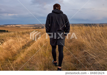 View from back on man walking in field after jogging, in sportive clothes 84801624