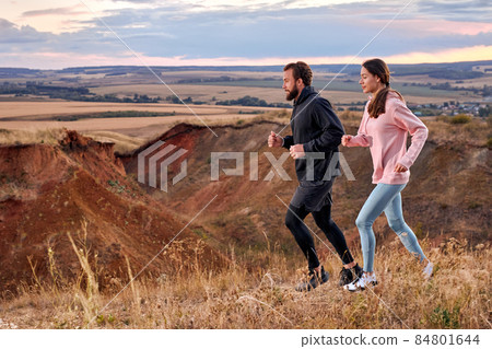 strong man and woman jogging along field outside the city at sunset, runners training strong man and woman jogging along field outside the city at sunset, runners training 84801644