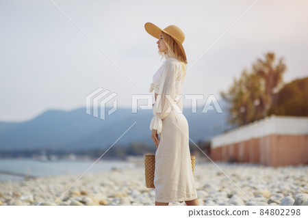 Woman in Elegant Beach Outfit Outdoors Against Palm Trees on the Background During Summer Vacations Woman in Elegant Beach Outfit Outdoors Against Palm Trees on the Background During Summer Vacations 84802298