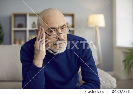 Portrait of strict reserved senior man in glasses sitting on couch with serious face, feeling skeptic, doubtful, uninspired and unexcited about bad idea or having secondhand embarrassment for somebody Portrait of strict reserved senior man in glasses sitting on couch with serious face, feeling skeptic, doubtful, uninspired and unexcited about bad idea or having secondhand embarrassment for somebody 84802856