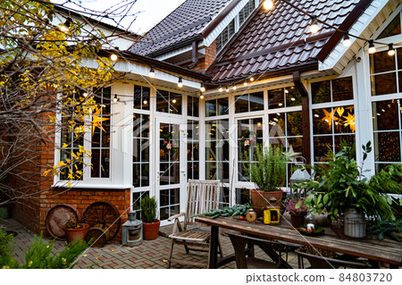 in evening. exterior of white house with large windows and garlands in courtyard 84803720